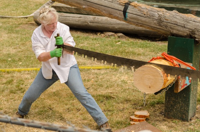 This woman was working very hard with her partner to saw through this log.
